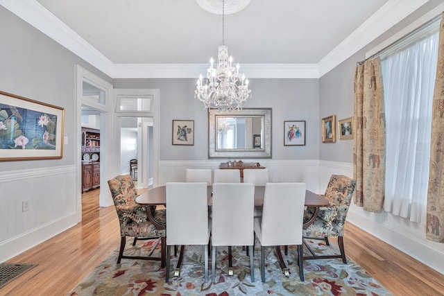 dining area with a healthy amount of sunlight, ornamental molding, a notable chandelier, and light wood-type flooring