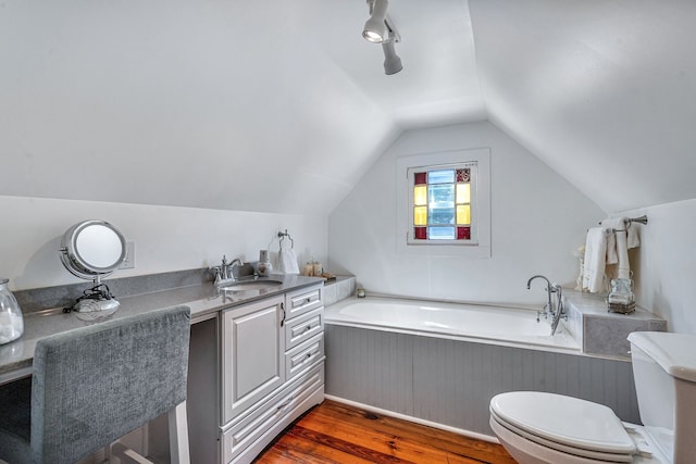 bathroom featuring a bathing tub, hardwood / wood-style floors, vaulted ceiling, toilet, and vanity