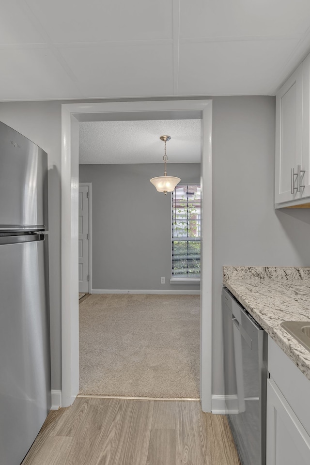 kitchen with appliances with stainless steel finishes, light stone counters, a textured ceiling, light hardwood / wood-style floors, and white cabinetry