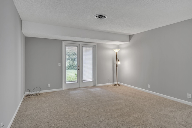 empty room featuring carpet floors, a textured ceiling, and french doors