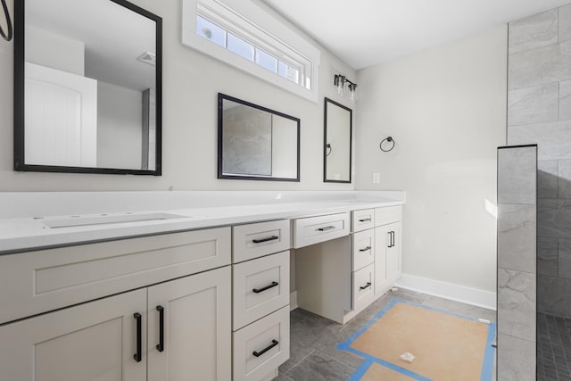 full bathroom with visible vents, baseboards, double vanity, tiled shower, and a sink