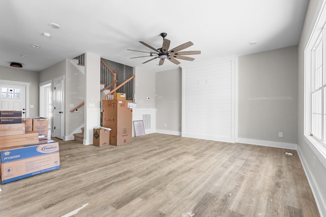 unfurnished living room with baseboards, stairs, ceiling fan, and wood finished floors