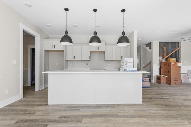 kitchen featuring decorative light fixtures, a center island, white cabinetry, light wood finished floors, and baseboards