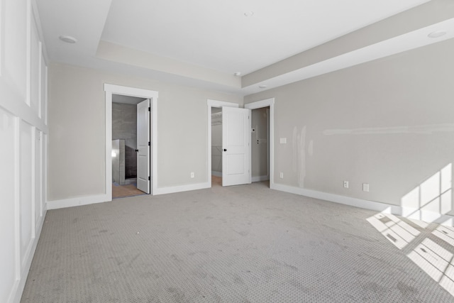 unfurnished bedroom featuring a tray ceiling, a spacious closet, light colored carpet, and baseboards