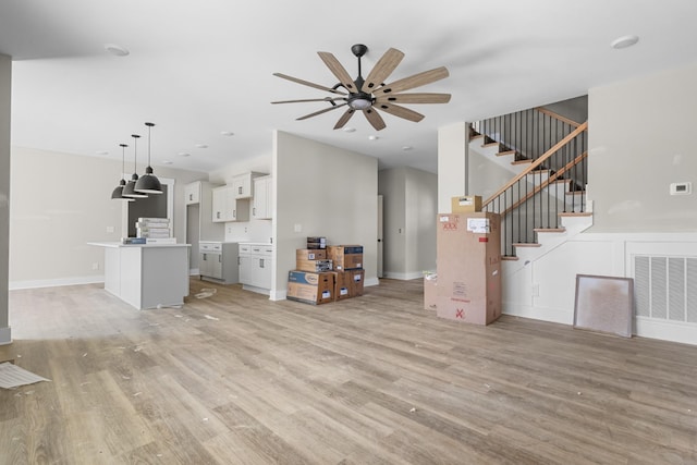 unfurnished living room with stairs, light wood-style flooring, a ceiling fan, and visible vents