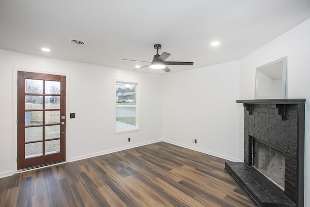 unfurnished living room with a wealth of natural light, ceiling fan, dark wood-type flooring, and a brick fireplace