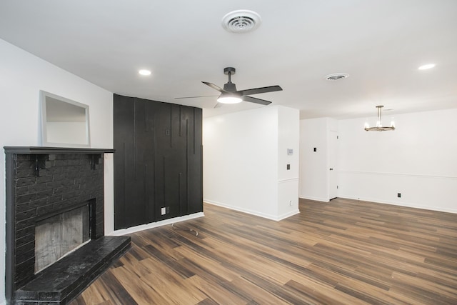 unfurnished living room with dark hardwood / wood-style floors, a fireplace, and ceiling fan with notable chandelier