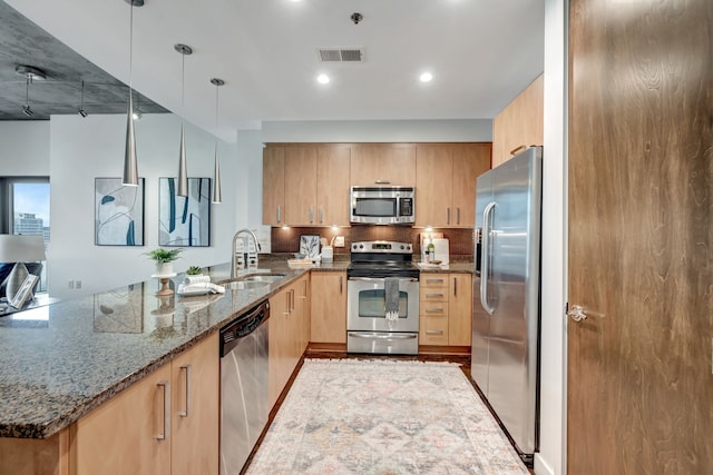 kitchen with hanging light fixtures, sink, dark stone countertops, appliances with stainless steel finishes, and kitchen peninsula