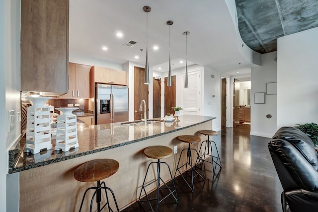 kitchen with light brown cabinets, hanging light fixtures, sink, stainless steel fridge, and dark stone countertops