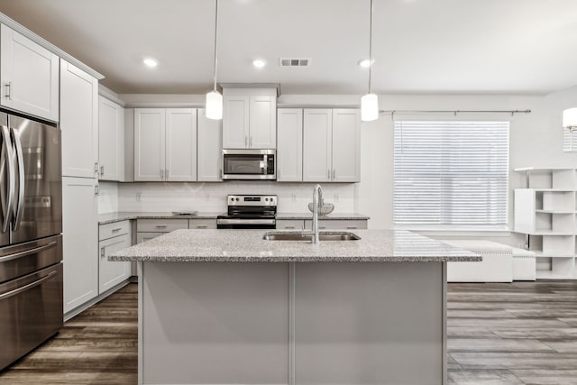 kitchen featuring sink, hanging light fixtures, light stone counters, an island with sink, and appliances with stainless steel finishes