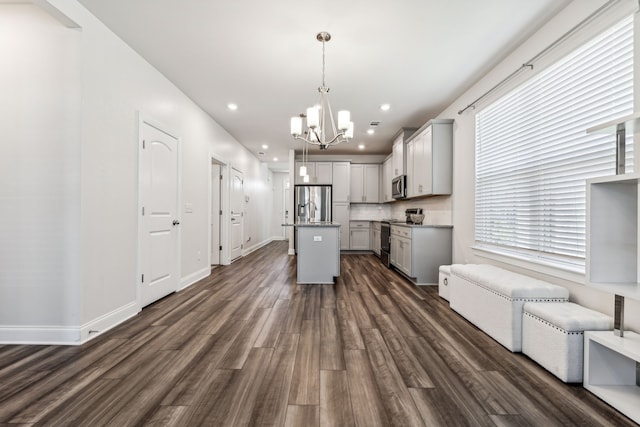 kitchen featuring backsplash, dark wood-type flooring, a center island with sink, decorative light fixtures, and stainless steel appliances