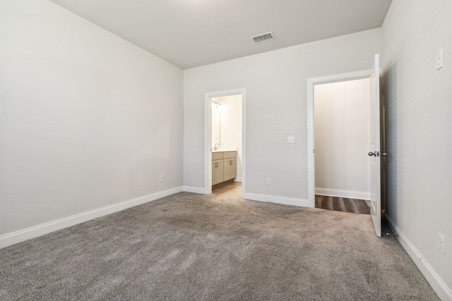 unfurnished bedroom featuring ensuite bathroom and light carpet