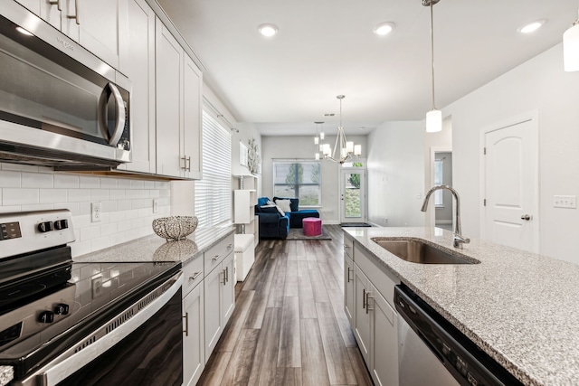 kitchen with light stone countertops, appliances with stainless steel finishes, dark hardwood / wood-style flooring, sink, and pendant lighting