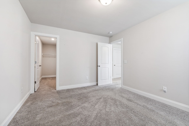 unfurnished bedroom featuring a walk in closet, light colored carpet, and a closet