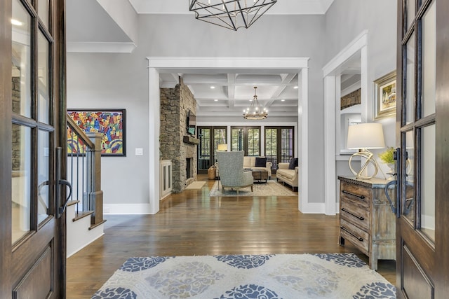 entrance foyer featuring coffered ceiling, a stone fireplace, dark hardwood / wood-style floors, beam ceiling, and a chandelier