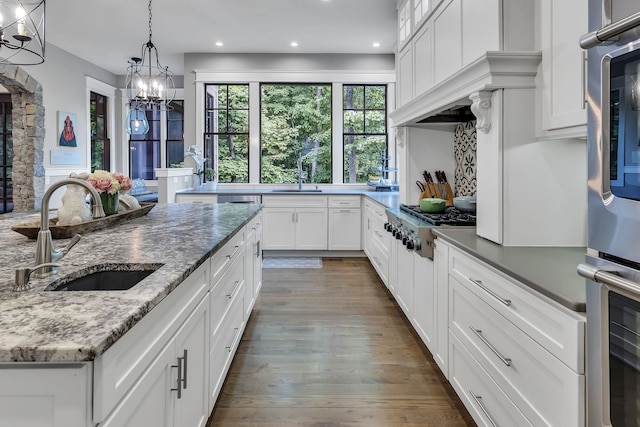 kitchen featuring white cabinets, sink, dark stone counters, and an inviting chandelier