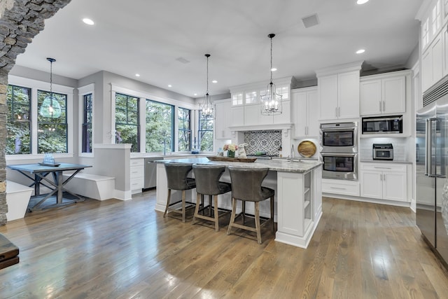 kitchen featuring light stone counters, built in appliances, an island with sink, wood-type flooring, and white cabinets