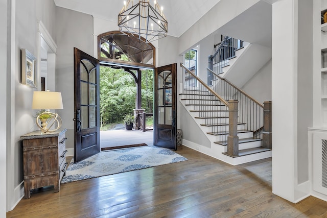 entryway with french doors, a towering ceiling, a notable chandelier, and hardwood / wood-style flooring