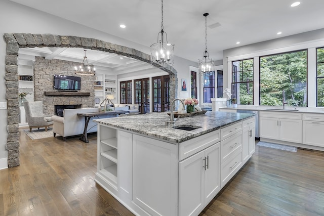 kitchen featuring a center island with sink, white cabinets, a stone fireplace, sink, and dark hardwood / wood-style floors