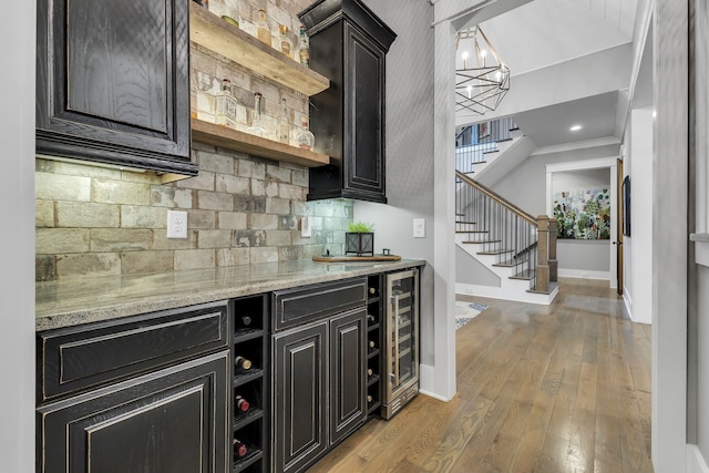 bar featuring hanging light fixtures, decorative backsplash, light stone countertops, light wood-type flooring, and beverage cooler