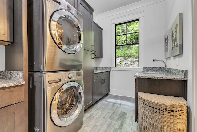 clothes washing area with cabinets, light wood-type flooring, stacked washer / drying machine, and sink