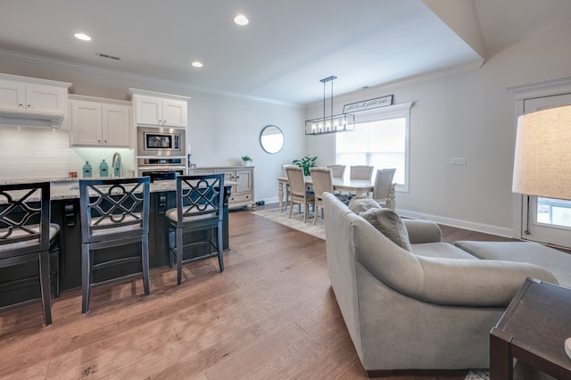 kitchen with appliances with stainless steel finishes, backsplash, light hardwood / wood-style flooring, white cabinetry, and hanging light fixtures