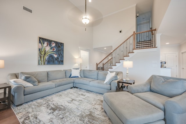 living room featuring ceiling fan, wood-type flooring, ornamental molding, and a high ceiling