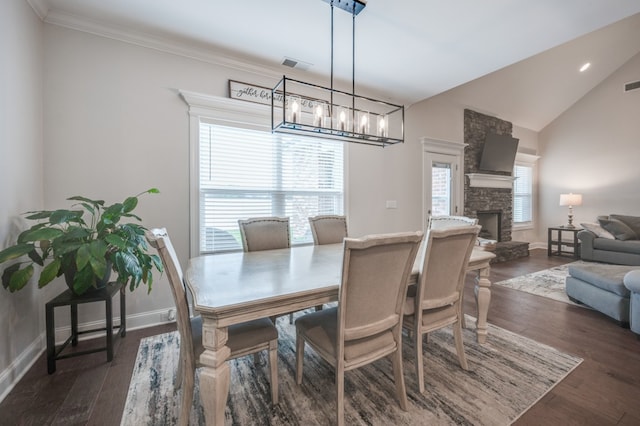 dining area featuring dark hardwood / wood-style flooring, a stone fireplace, lofted ceiling, and crown molding