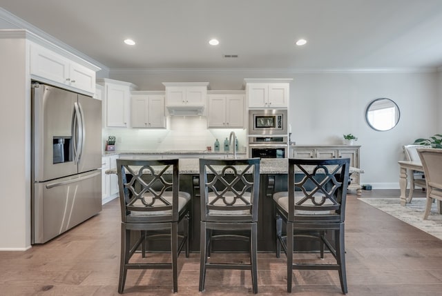 kitchen featuring a kitchen breakfast bar, light wood-type flooring, stainless steel appliances, white cabinets, and an island with sink