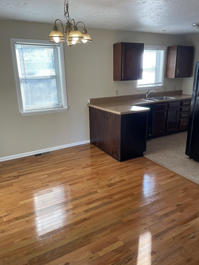 kitchen featuring black refrigerator, light hardwood / wood-style flooring, a textured ceiling, and an inviting chandelier