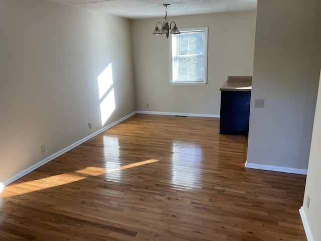 unfurnished dining area featuring dark hardwood / wood-style flooring, a chandelier, and a textured ceiling