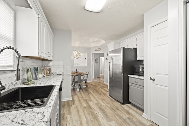 kitchen featuring appliances with stainless steel finishes, light wood-type flooring, backsplash, a textured ceiling, and white cabinetry