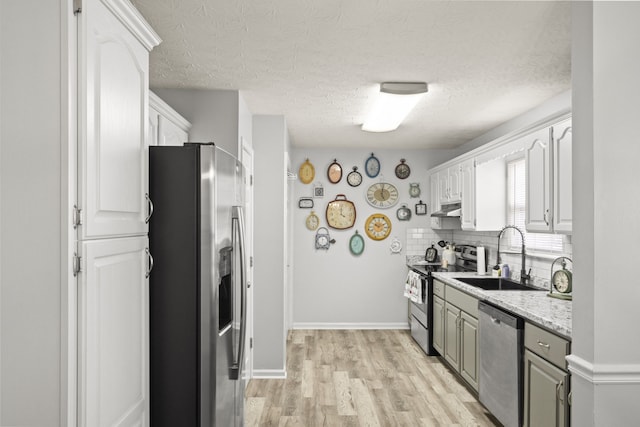 kitchen with backsplash, sink, light wood-type flooring, appliances with stainless steel finishes, and white cabinetry