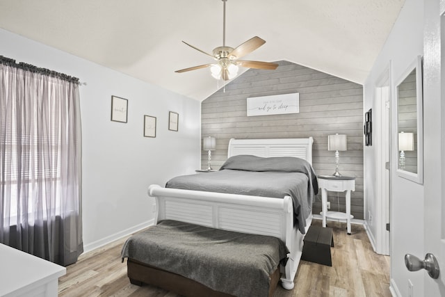 bedroom featuring ceiling fan, light wood-type flooring, lofted ceiling, and wooden walls