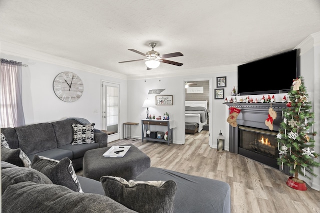 living room featuring crown molding, ceiling fan, a textured ceiling, and light wood-type flooring