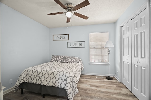 bedroom with a textured ceiling, a closet, light hardwood / wood-style floors, and ceiling fan