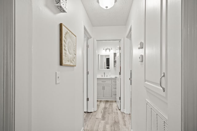 hallway featuring light hardwood / wood-style flooring, a textured ceiling, and sink