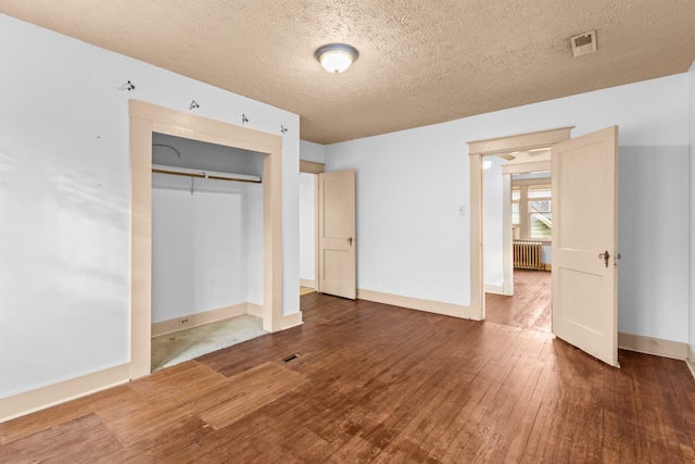 unfurnished bedroom with a textured ceiling, dark hardwood / wood-style flooring, a closet, and radiator