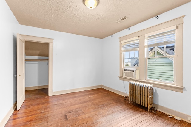 unfurnished bedroom featuring radiator heating unit, cooling unit, wood-type flooring, a textured ceiling, and a closet