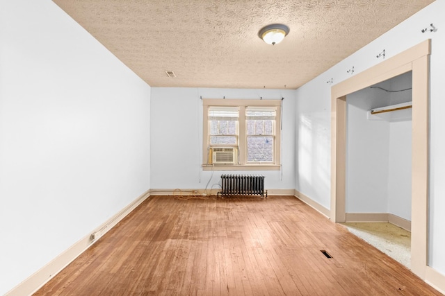 unfurnished room featuring cooling unit, wood-type flooring, a textured ceiling, and radiator