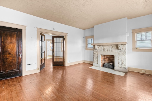 unfurnished living room with hardwood / wood-style flooring, french doors, a fireplace, and a textured ceiling