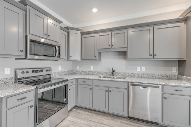 kitchen featuring appliances with stainless steel finishes, light wood-type flooring, light stone counters, gray cabinetry, and sink