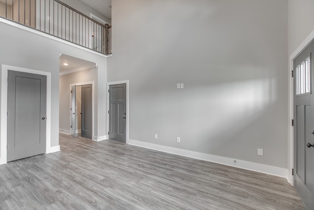 foyer entrance with light wood-type flooring, a towering ceiling, and ornamental molding