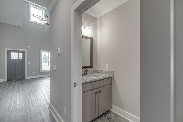 bathroom featuring vanity, a high ceiling, crown molding, ceiling fan, and wood-type flooring