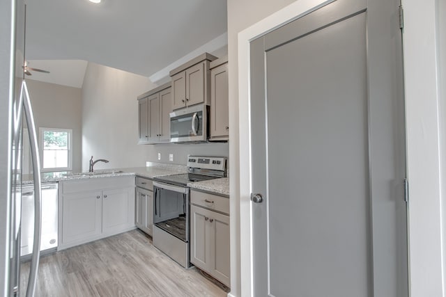 kitchen featuring sink, light hardwood / wood-style flooring, ceiling fan, light stone countertops, and appliances with stainless steel finishes