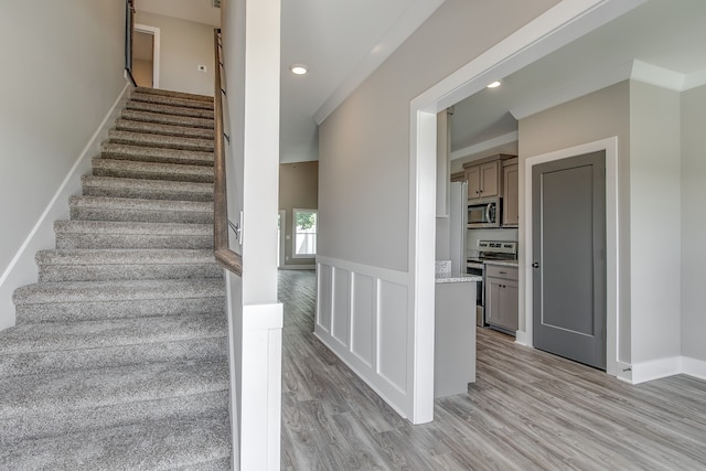 staircase with wood-type flooring and ornamental molding