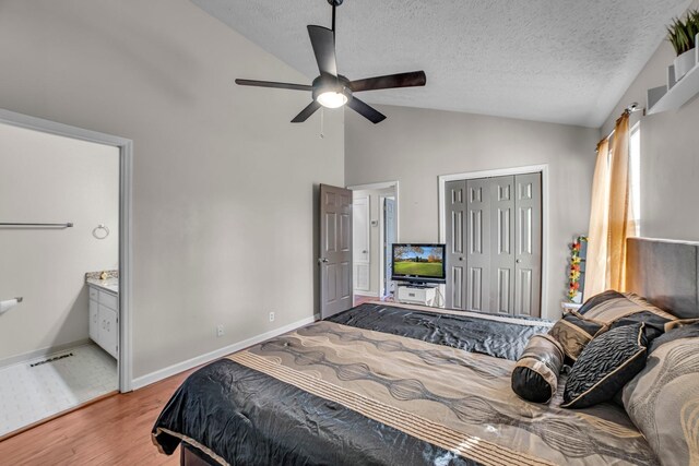 bedroom featuring light wood-type flooring, ensuite bath, a textured ceiling, vaulted ceiling, and ceiling fan