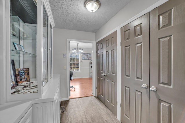 hall with a textured ceiling, light hardwood / wood-style floors, and an inviting chandelier