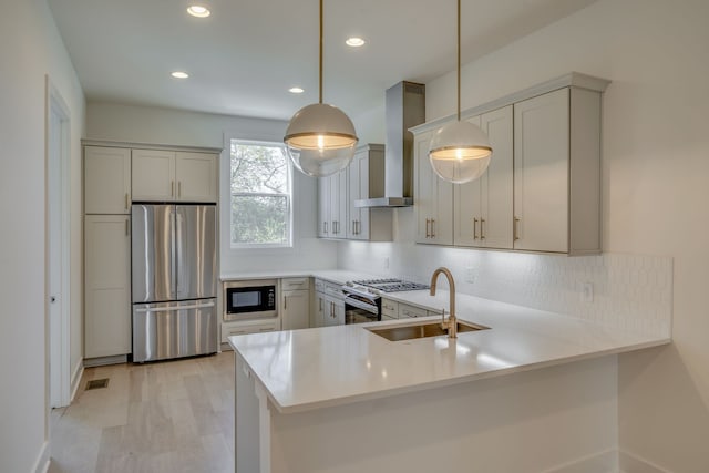 kitchen with sink, hanging light fixtures, wall chimney exhaust hood, appliances with stainless steel finishes, and kitchen peninsula