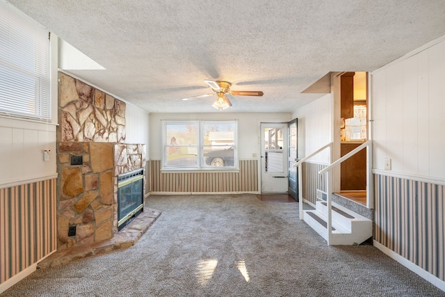 unfurnished living room featuring a stone fireplace, ceiling fan, carpet floors, and a textured ceiling